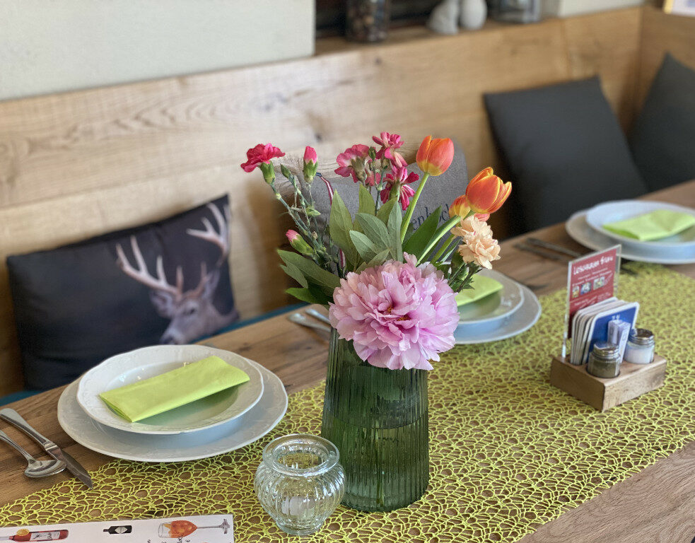 gedeckter Tisch mit Blumen Tulpen, grünem Läufer, Teller mit Servietten, dahinter Polster mit Hirschdruck